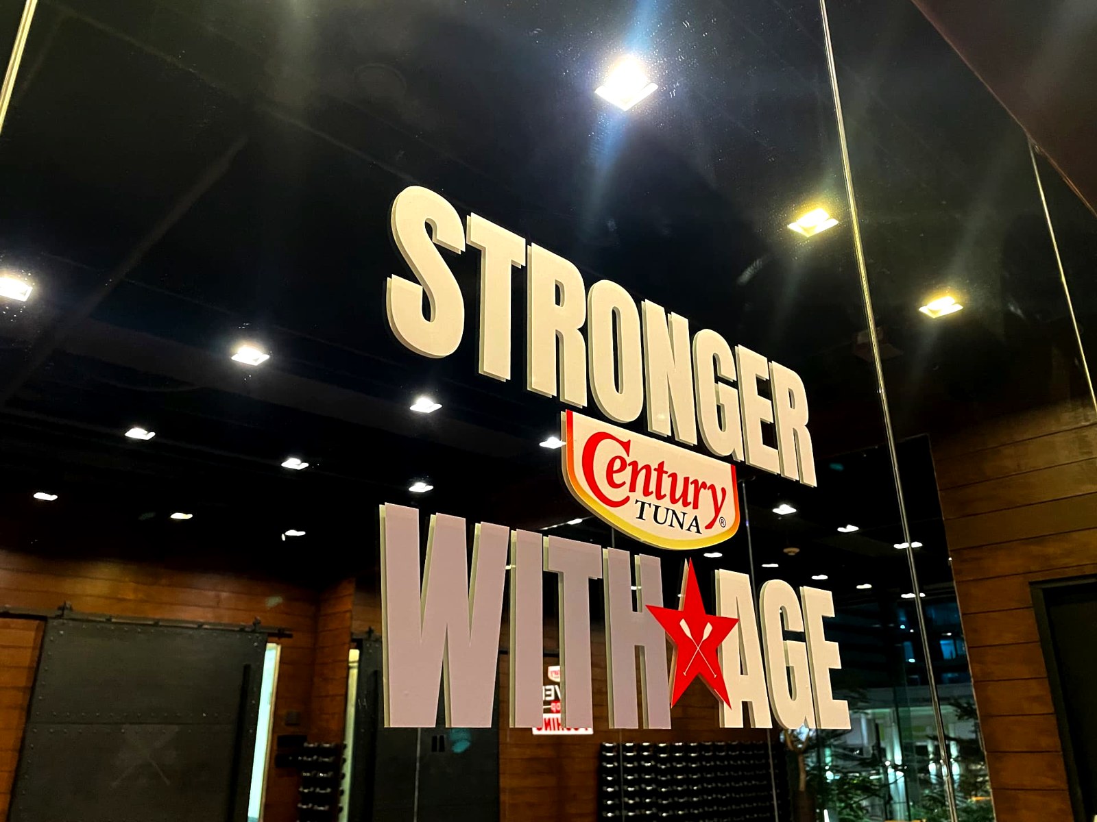 Century Tuna Stronger with Age signage reflected in a studio glass wall
